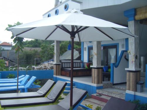 a white umbrella sitting on a patio with lounge chairs at De Adema Guesthouse in Amed