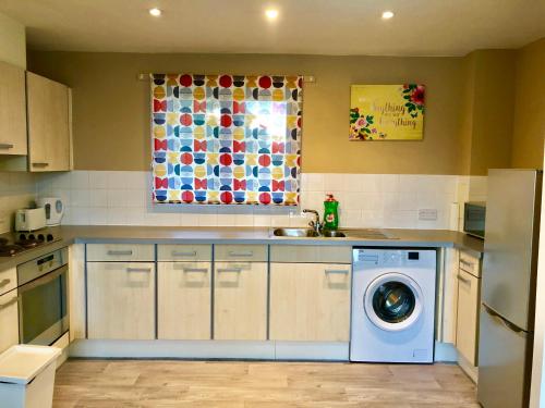 a kitchen with a washing machine and a window at 2 Bedrooms Modern Apartment, Lounge, Full Kitchen, Balcony, 5 minutes Stratford Station in London
