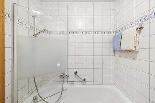a white tiled bathroom with a tub and a shower at Fewo Brünnstein - Nr 28 Pool, Sauna in Oberaudorf