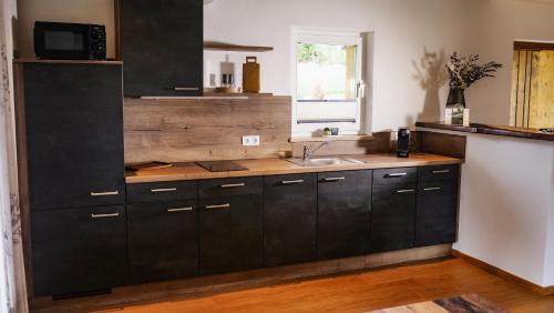 a kitchen with black cabinets and a sink at Franz Josefs Wald-Chalets in Untergriesbach