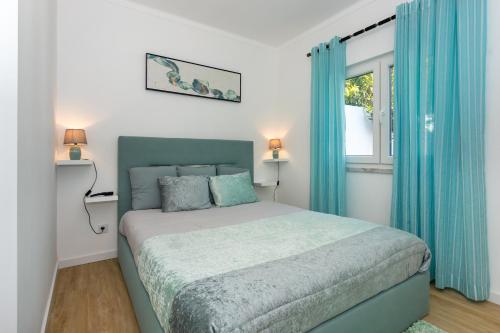 a bedroom with a bed with blue curtains and a window at Refúgio Das Barcas in Lourinhã