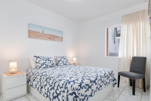 a white bedroom with a bed and a chair at Vistamar in Puerto del Carmen