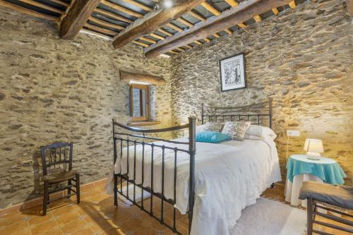 a bedroom with a bed and a stone wall at Casa El Portón, Bubión in Bubión