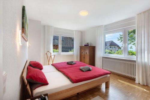 a bedroom with a bed with red sheets and two windows at Familie Quednow - Im Algi in Görwihl