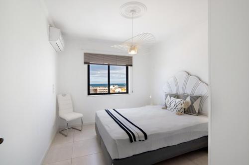 a white bedroom with a bed and a chair at Lindo T2 com vista mar in Quarteira