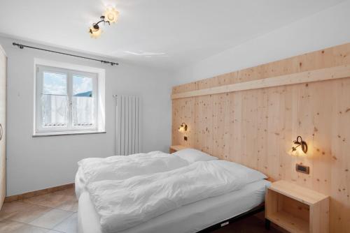 a bedroom with a white bed and a wooden wall at Piaz de Vich in Vigo di Fassa