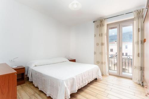 a white bedroom with a bed and a large window at Cozy And Cool Flat in Orosei