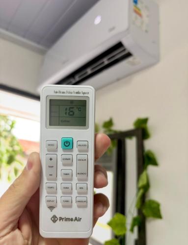 a person holding a remote control in front of a microwave at Mini Suite - Pousada Lemon com Cozinha - Sesc Bertioga - Ar Condicionado e Frigobar in Bertioga