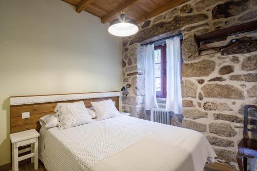 a bedroom with a bed and a stone wall at C Vilamide in Parada de Achas
