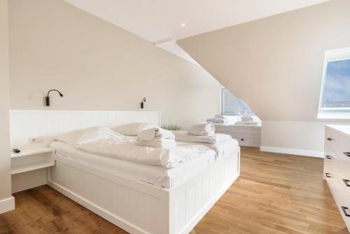 a white bedroom with a large white bed and wooden floors at Strandburg in Westerland