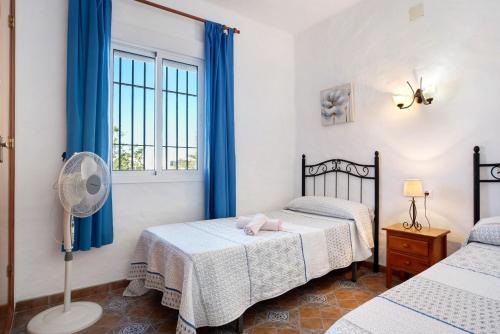 a bedroom with two beds with blue curtains and a fan at Las Calas de Roche in Roche