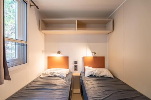 two beds in a small room with a window at Mobilhome au Camping La Yole in Vendres