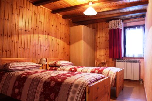 three beds in a room with wooden walls and a window at Maison Leveque in Brusson