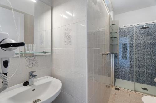 a white bathroom with a shower and a sink at Apartamentos Playa Azul - 7 in Vallehermoso