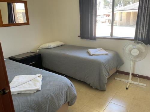 a room with two beds and a fan and a window at Unit 16, 2 Casuarina Crescent, Ocean Beach Chalets in Jurien Bay