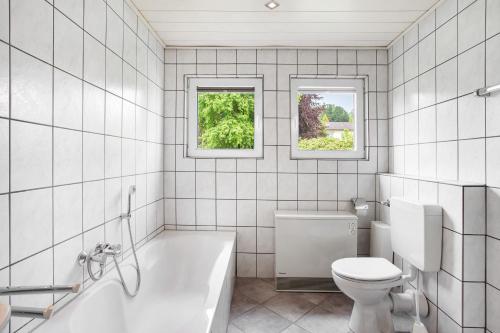 a bathroom with a tub and a toilet and two windows at Ferienwohnung Triska in Balve