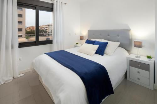 a white bedroom with a blue and white bed and a window at Playamarinsa in Torre del Mar