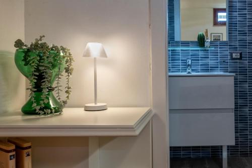 a table with a lamp and a green vase with a plant at Villa Olivetta con piscina in Alghero