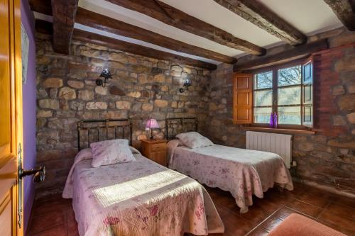 a bedroom with two beds and a stone wall at Apartamento Juntana 1 in Villacarriedo