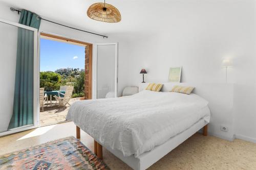 a white bedroom with a bed and a large window at Rez de villa avec jardin vue mer in Fréjus