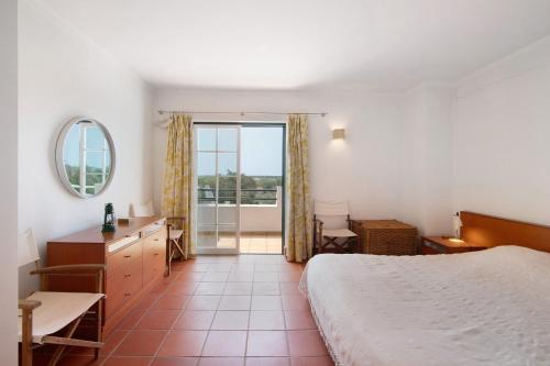 a bedroom with a bed and a desk and a balcony at Casa do Ouriço - Cabanas Tavira in Tavira