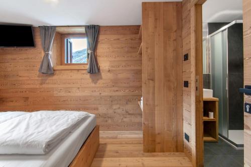 a bedroom with a wooden wall with a bed and a window at Agriturismo Montespluga in Madesimo