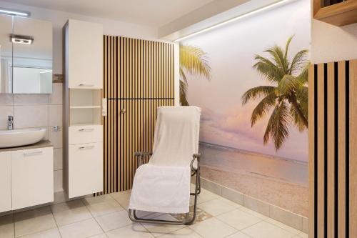 a bathroom with a white chair and a palm tree mural at Ferienwohnung Hörnleberg in Gutach im Breisgau
