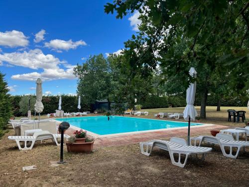 a swimming pool with white chairs and umbrellas at Il Forcone in Panicale
