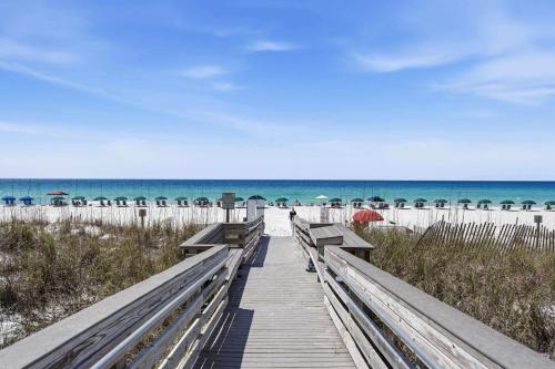 a wooden boardwalk leading to the beach with umbrellas at Gulf Front condo with Beach access and shared Pool in Fort Walton Beach