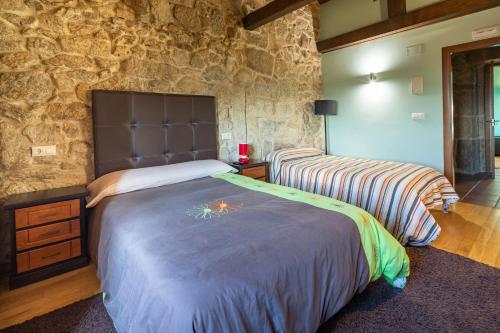 a bedroom with two beds and a stone wall at Lugar Da Xacra in Meder