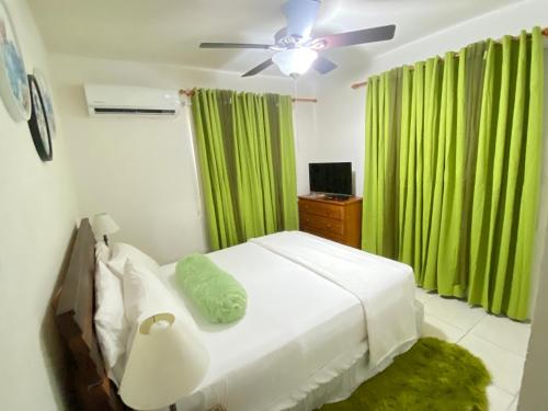 a bedroom with a bed with a ceiling fan and green curtains at Cool Stay in Christ Church