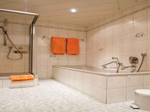 a bathroom with a tub and a shower with orange towels at Gästehaus Herrmann in Bad Rippoldsau-Schapbach