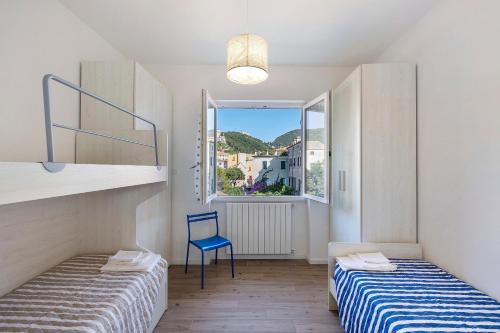 two beds in a room with a blue chair and a window at Il Borgo Incantato con garage in Finale Ligure