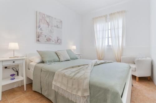 a white bedroom with a bed and a chair at Calida Vivienda Accesible in Caleta De Fuste
