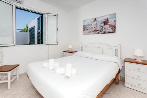 a white bedroom with a white bed and a window at Villa Goyo in Cala en Bosc