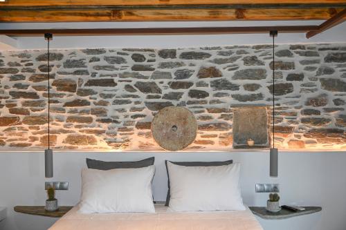 a stone wall behind a bed with white pillows at Celini Villas Tinos in Tinos