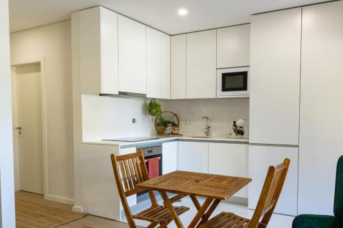 a kitchen with white cabinets and a wooden table and chairs at Aurora do Furadouro l in Ovar