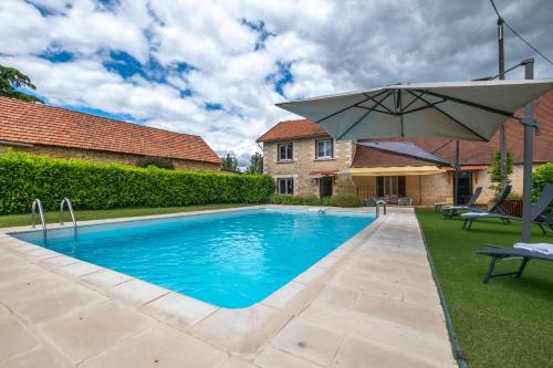 a swimming pool with an umbrella next to a house at Maison familiale à Archignac in Archignac