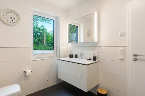 a white bathroom with a sink and a clock at Ferienwohnung Viedenz in Drolshagen