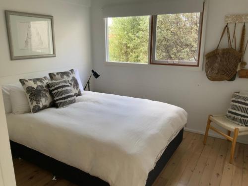 a bedroom with a white bed with pillows and a window at The G Shack at Rennies Beach in Ulladulla