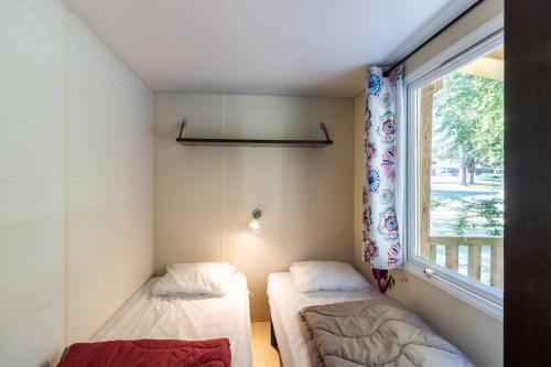 two beds in a small room with a window at Mobilhome Le Cocon in Saint-Pompont