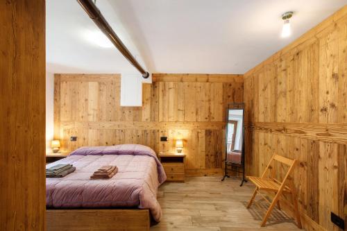 a bedroom with wooden walls and a bed and a chair at Les Cles - Achillea in Valsavarenche