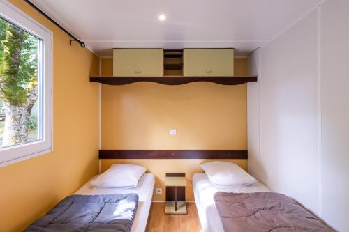 two beds in a room with a window at Mobilhome Le Tilleul in Saint-Pompont