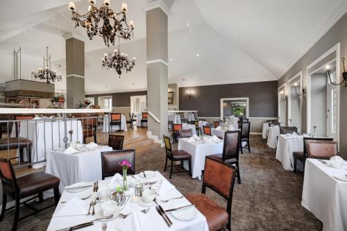 a restaurant with white tables and chairs and a chandelier at Mount Grace Hotel & Spa in Magaliesburg