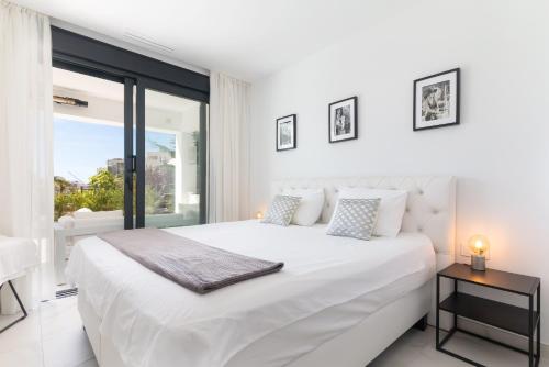 a white bedroom with a large white bed and a window at Ground floor 2bed Miradores del Sol in Estepona