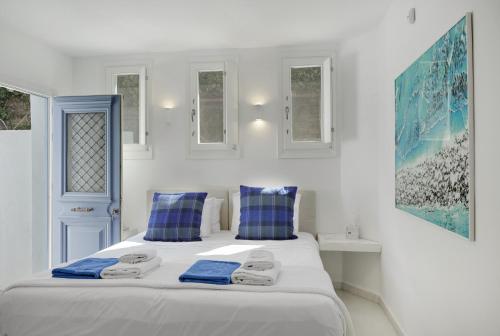 a white bedroom with a large bed with blue pillows at Blueros - Main Villa in Megas Gialos - Nites