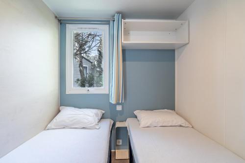 two beds in a small room with a window at Mobilhomelaco34 in Vendres