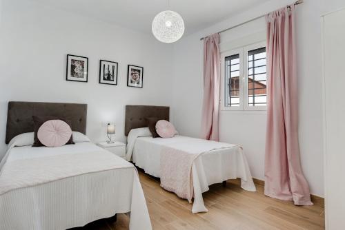 two beds in a white room with pink curtains at Villa Sandra solo familias in Cádiz