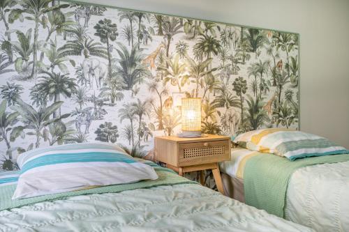 a bedroom with two beds and a wallpaper with palm trees at le chai de la lumineuse in Saint-Pierre-dʼOléron