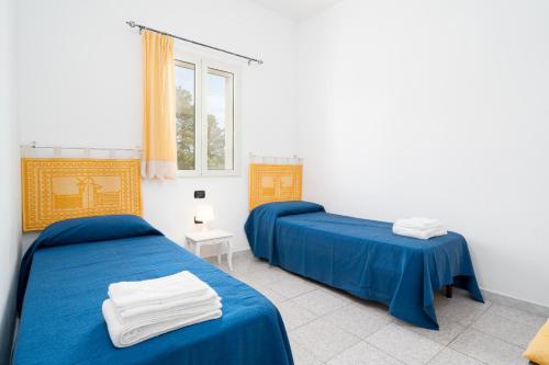two beds in a room with blue sheets and a window at Villa Sa Mela 28 in Orosei